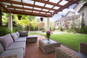 A backyard patio with a wooden awning above and a green yard in the background.
