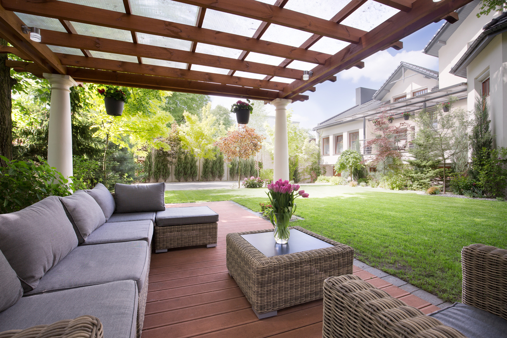 Patio furniture underneath a pergola with a green backyard in the background
