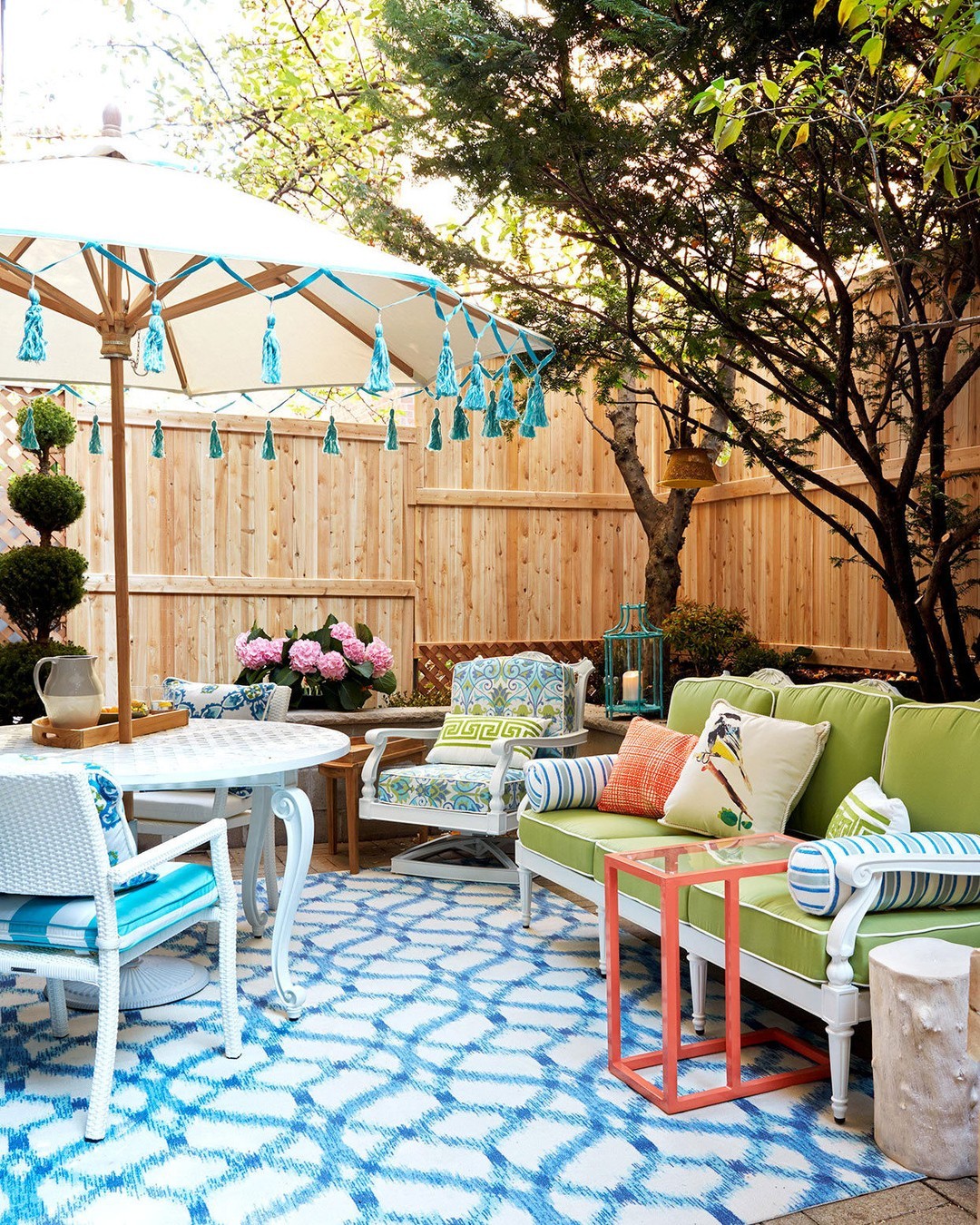 A colorfully decorated backyard patio area with couches and a standing umbrella. Photo by Instagram user @betterhomesandgardens