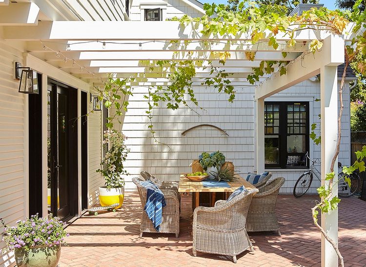 Patio furniture on a wooden deck beneath a trellis covered in a vining plant. Photo by Instagram user @fergusgarber.
