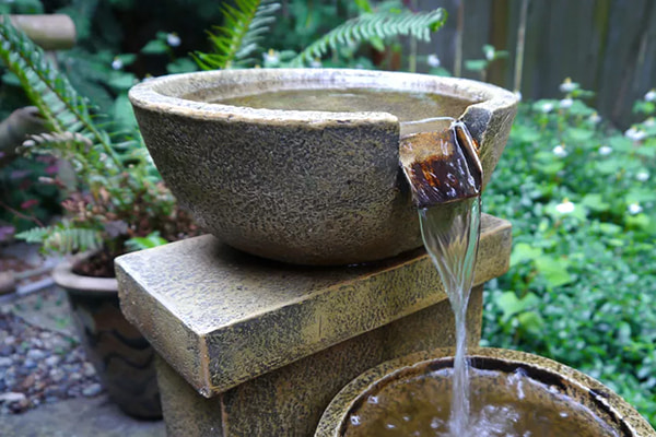 Stone bowl water fountain in front of green ground cover