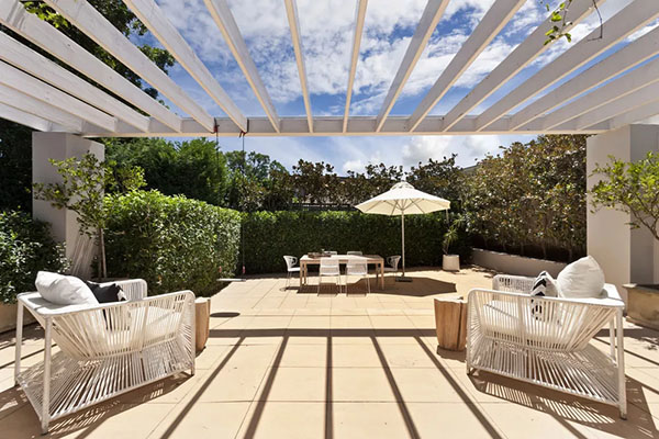 White pergola and furniture on concrete deck with privacy hedges