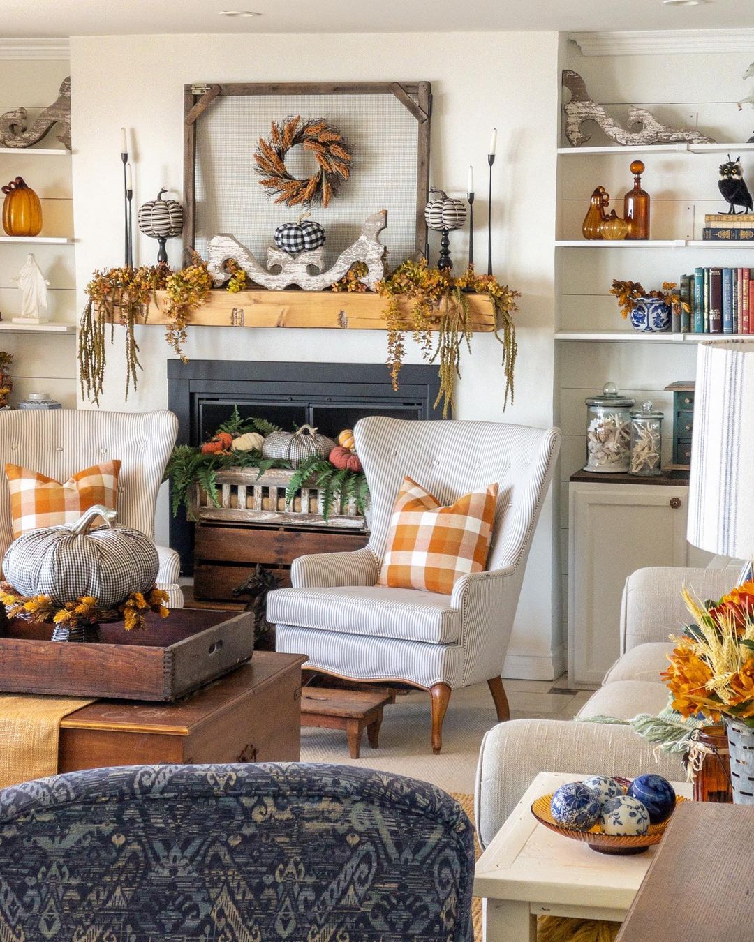 Living room with a chair in front of a fireplace and a mantle decorated with autumnal foliage. Photo by Instagram user @upsydaisycottage. 