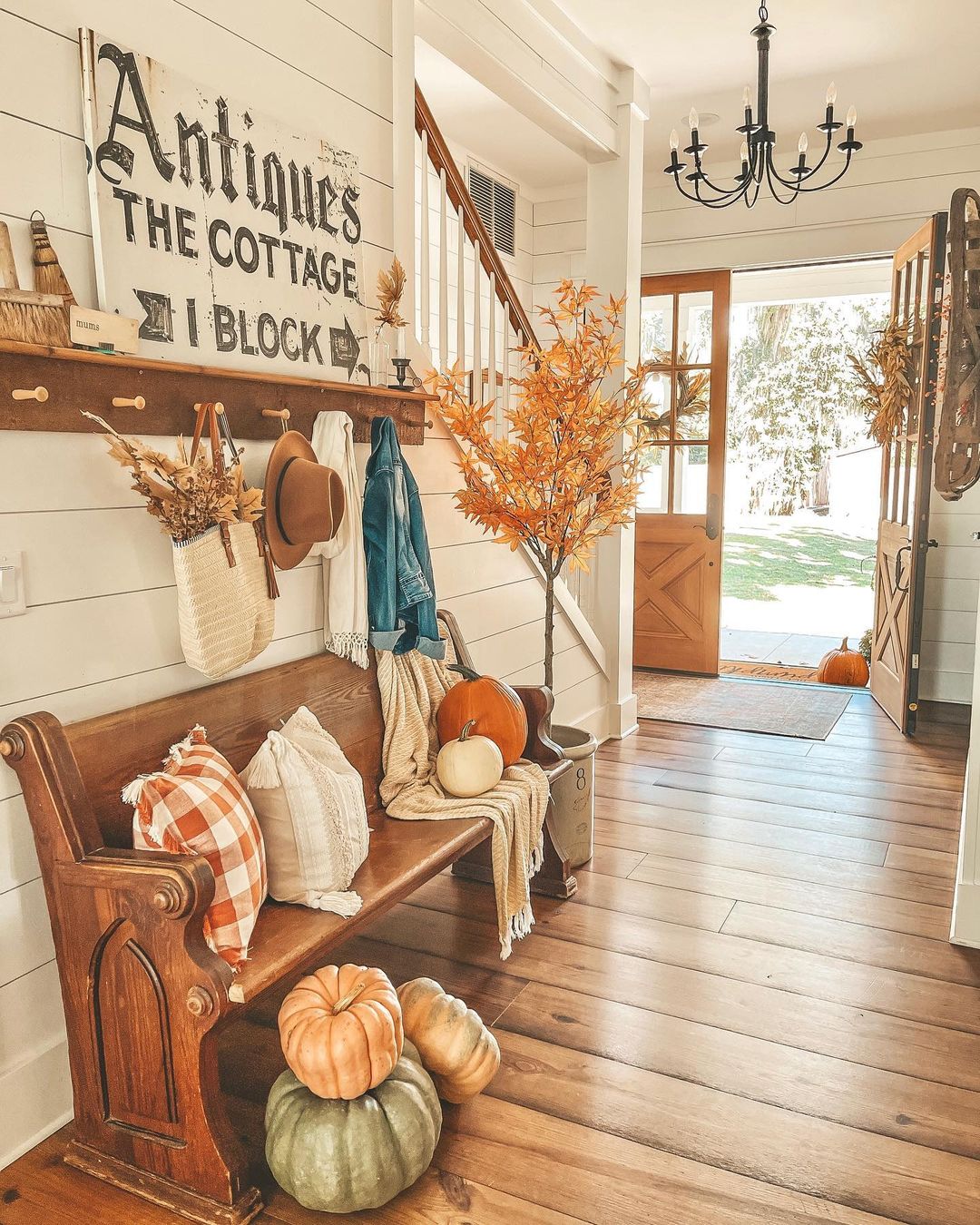 A farmhouse-style entryway with a bench, pegboard for coats and hats, and an open front door. Photo by Instagram user @lakefrontfarmhouse.