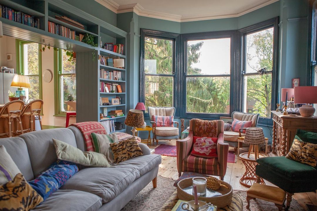 Turquoise living room with large windows, couches, chairs, and built in bookcase. Instagram photo by @thehouseupstairs