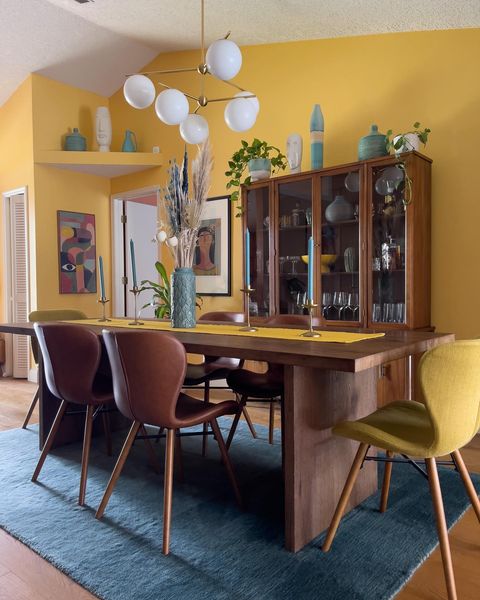 A kitchen with yellow painted walls, and a nice dining table with a yellow table cloth on top.