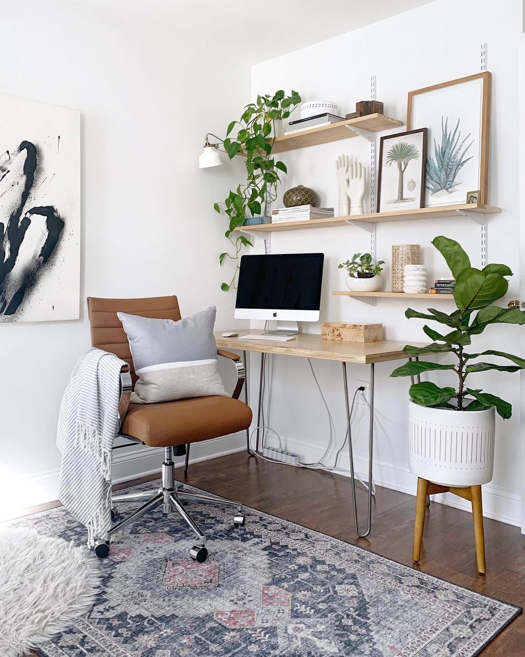 A light, bright home office space with a wooden desk and shelving on the wall above it. Photo by Instagram user @kcdesignco.