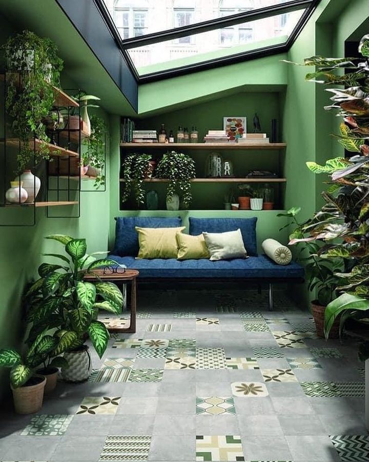 A vibrant green room with a couch and many house plants throughout the space. There is a skylight above. Photo by Instagram user @yourfavoriterealtorlv.
