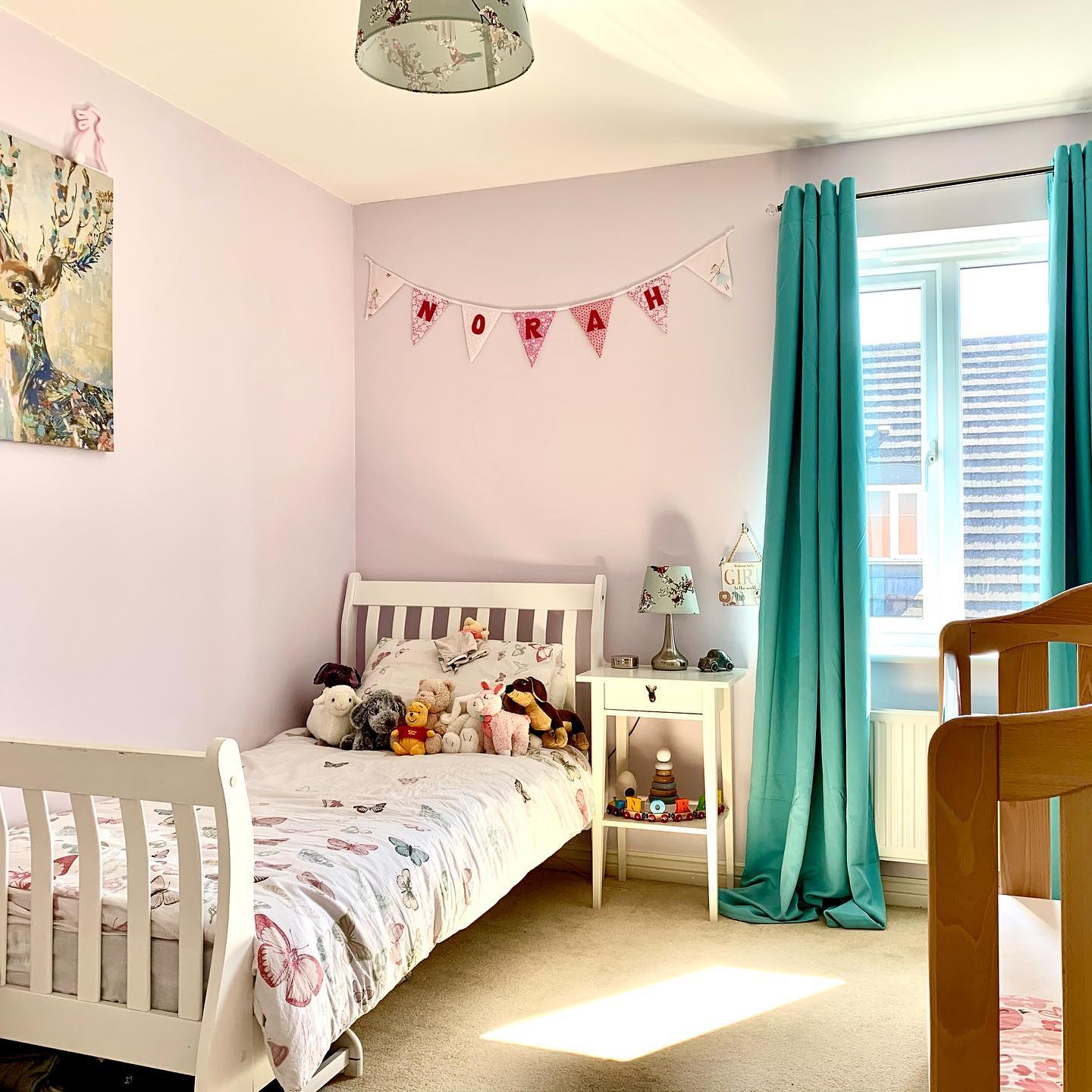 A lilac painted kids room with stuffed animals on the bed.