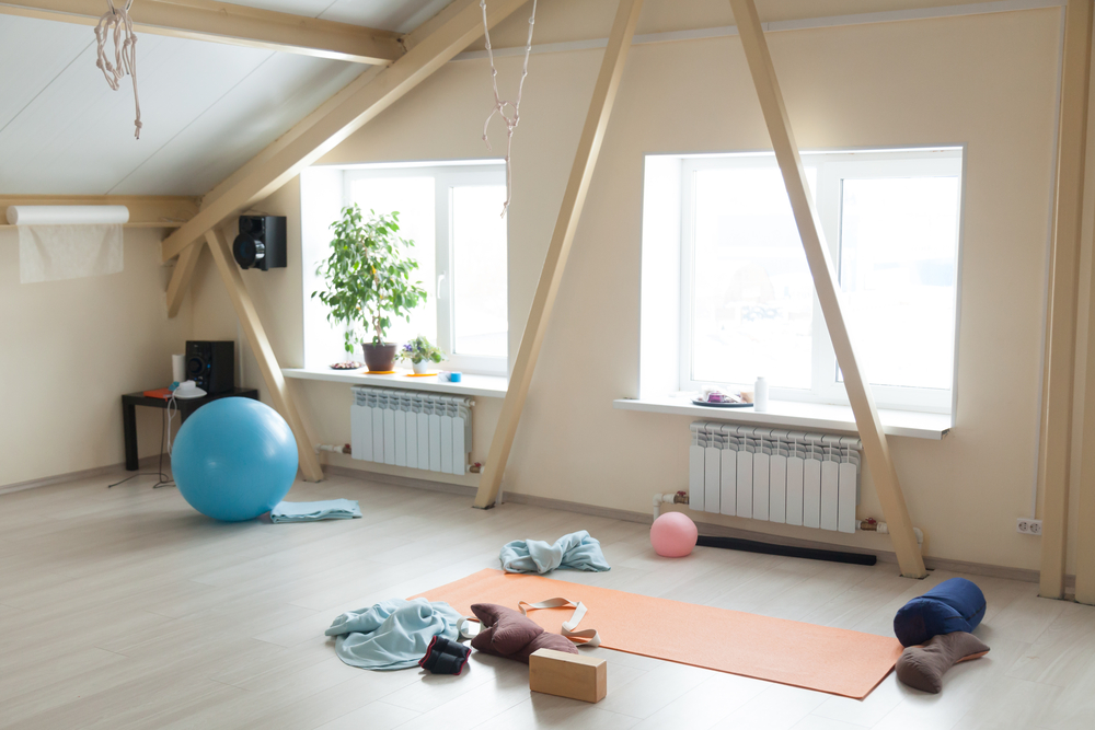 Well-lit home yoga studio with windows, a yoga mat, an exercise ball, and other yoga equipment