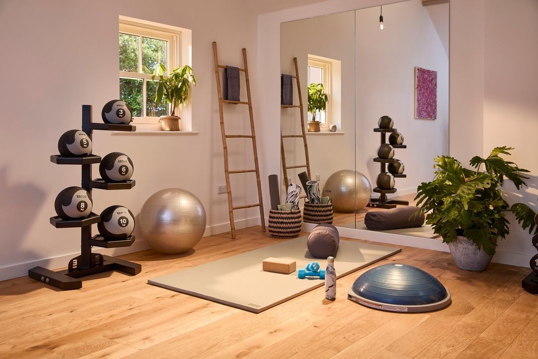 A home gym with a medicine ball rack, wall mirrors, and yoga equipment on the floor. Photo by Instagram user @motive8group