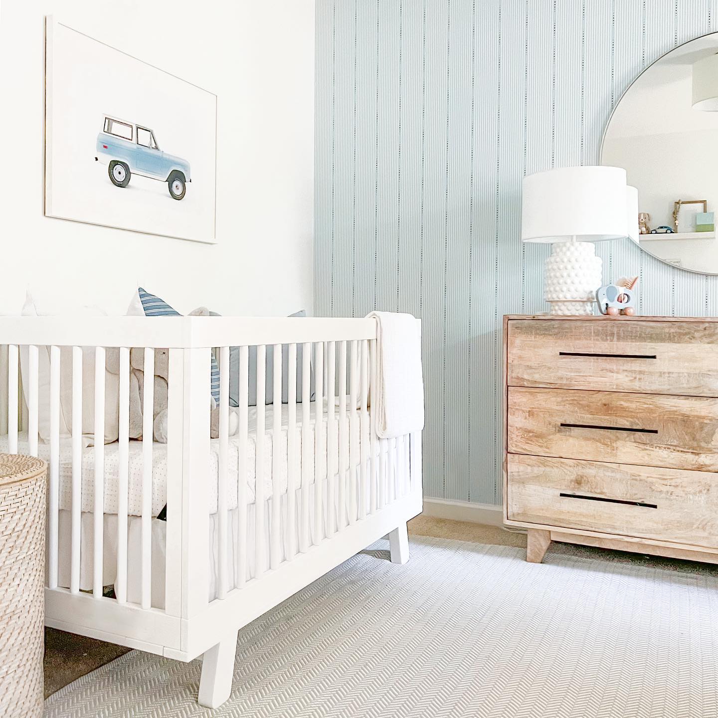 A soft blue nursery with an illustration of a truck behind the crib. Photo by Instagram user @thesimplewhitehome.