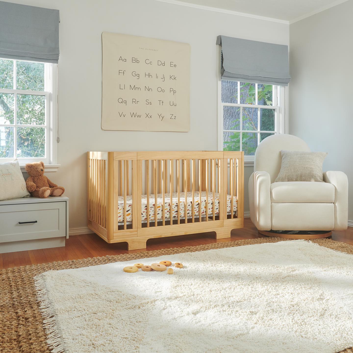 Nursery with wooden convertible crib, large rug, and alphabet wall hanging. Photo by Instagram user @babyletto