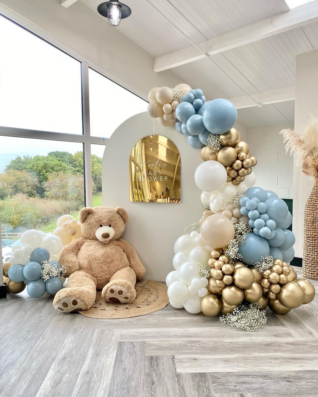 A large teddy bear and balloons are pictured in a baby shower venue. Photo by Instagram user @lunamoonballoons.