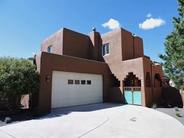 Reddish-tan Adobe-style home with white garage and turquoise fence. Photo by Instagram user @realestateassociatesnm.