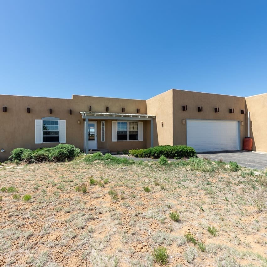 Single-level, tan Adobe-style home with desert landscape. Photo by Instagram user @coldwellbankersantafe.