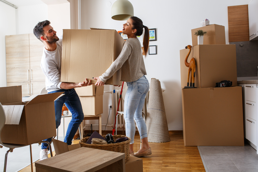 Two people carry a box through a packed-up room.