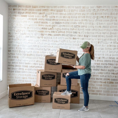 A women standing holding an Extra Space Storage moving back in front of a stack of moving boxes