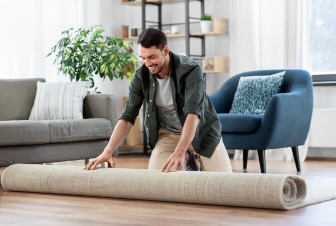 A picture of a man rolling up a carpet in his living space.