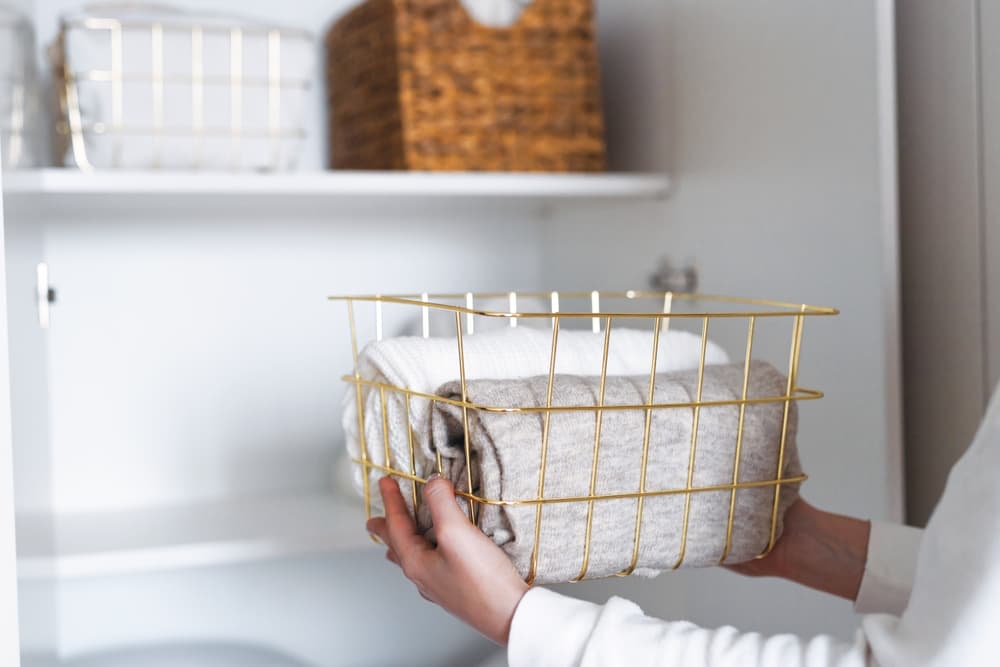 A person placing a basket of towels in an organized closet.