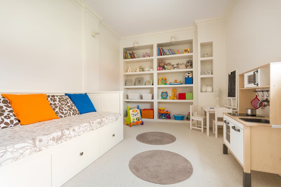 A clean kids playroom with large built-in shelves, a built-in bench seat with storage, and a play kitchen set.