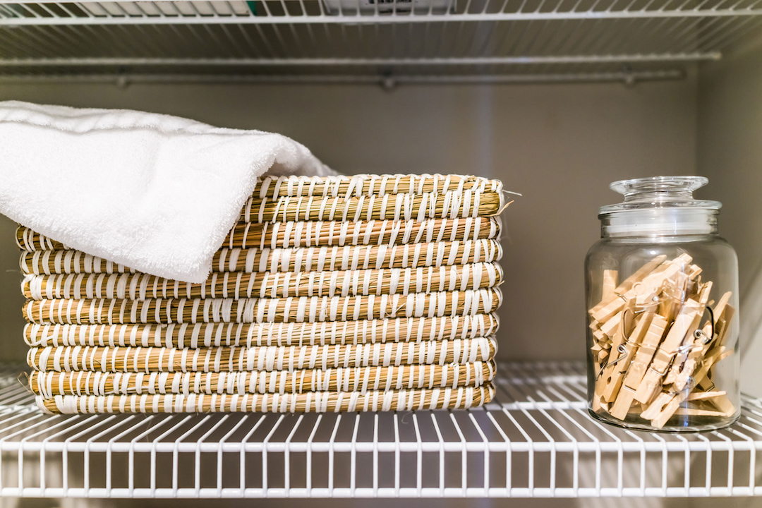 A wicker basket holding a white towel and a glass jar filled with wooden clothespins