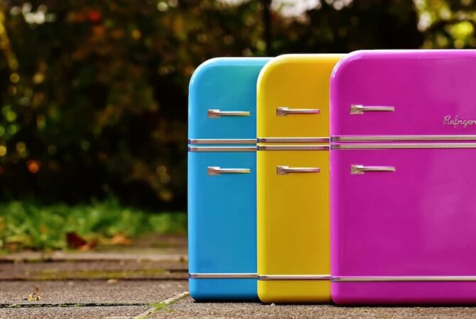 A pink, yellow, and blue refrigerator on a sidewalk