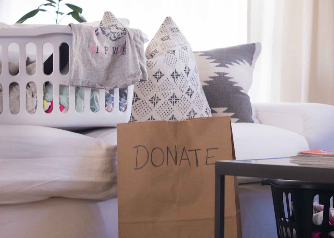 A laundry basket and paper bag labeled "Donate" filled with items.