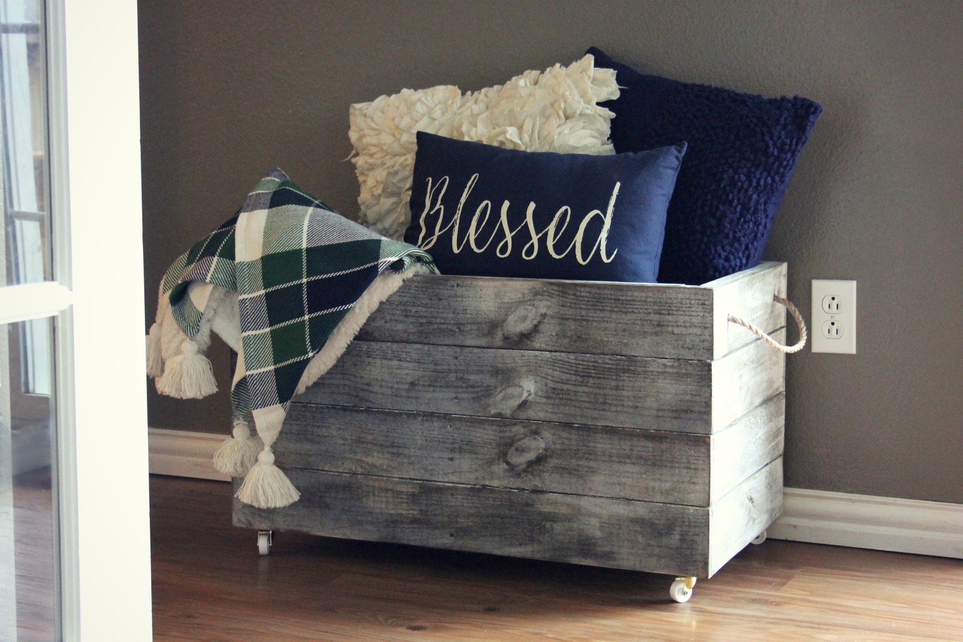Pillows and blankets are stored in a wooden crate with wheels.