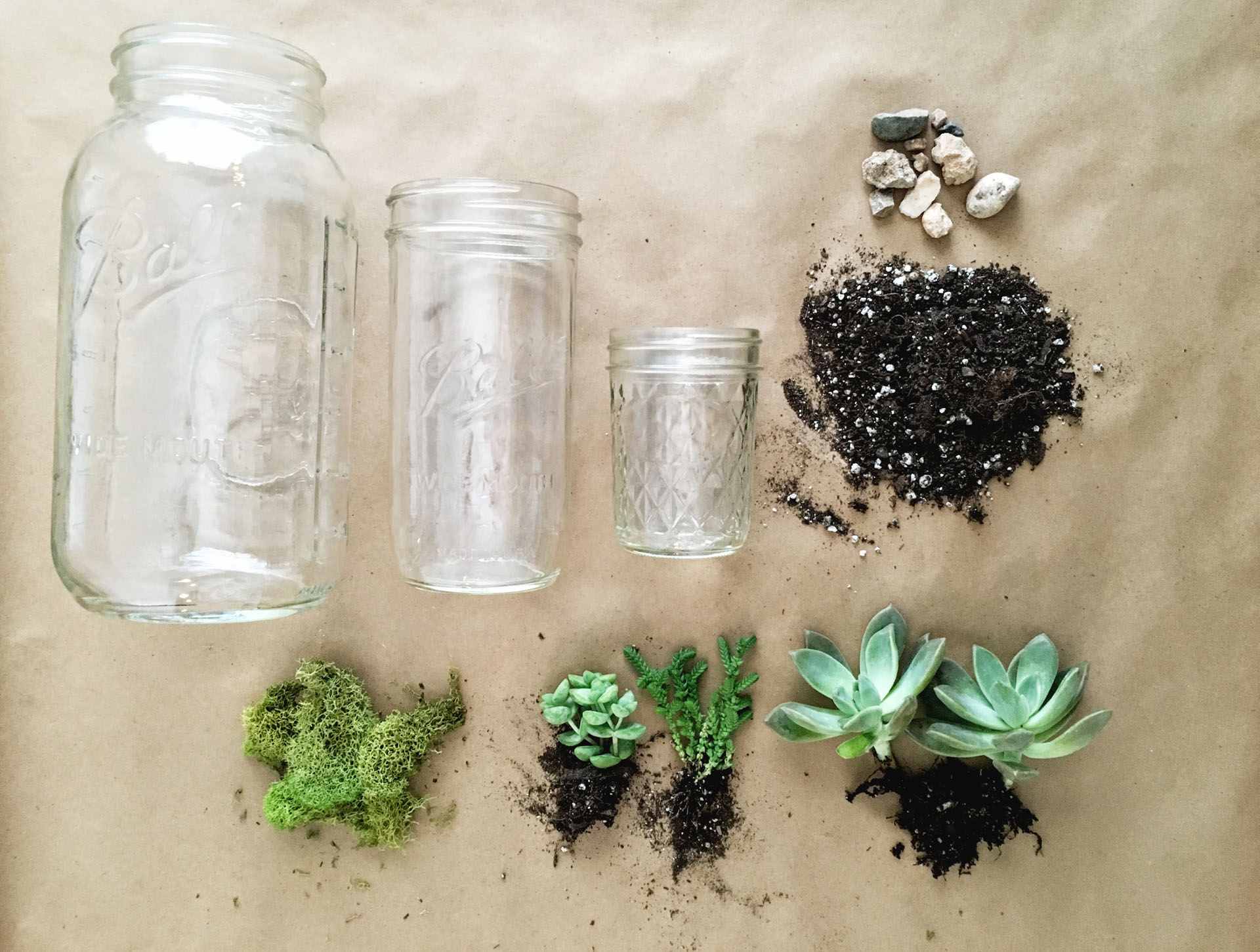 Three glass draws lay flat near a pile of dirt, rocks, and succulents.