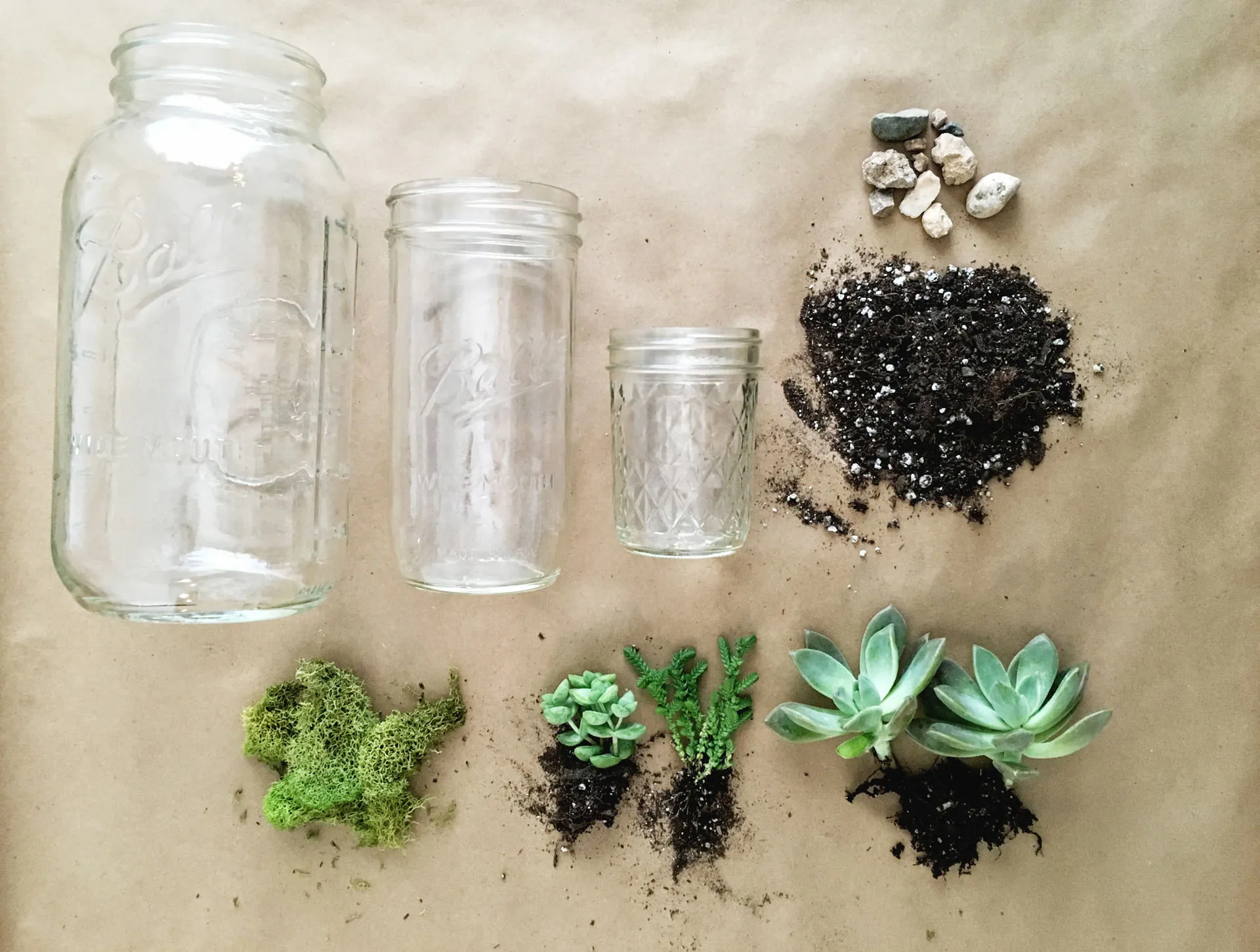 Three glass draws lay flat near a pile of dirt, rocks, and succulents.