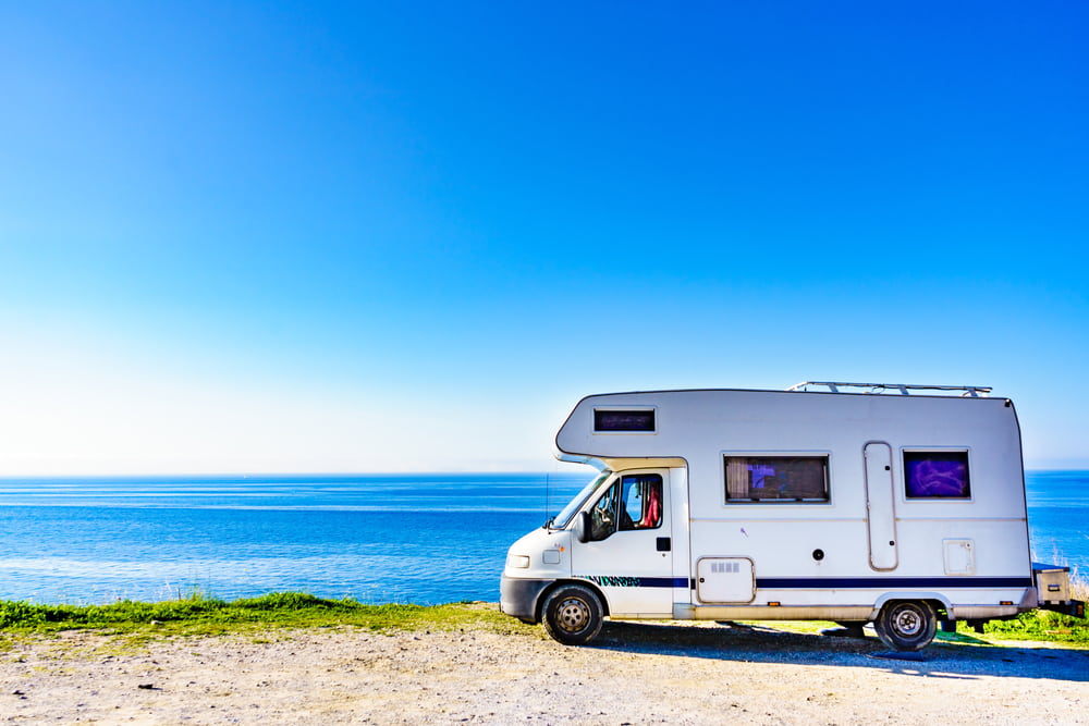 Camper parked in front of ocean during daytime.
