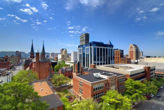 Skyline of Birmingham, AL complete with a clear sky, brick buildings, and lush trees in the foreground.