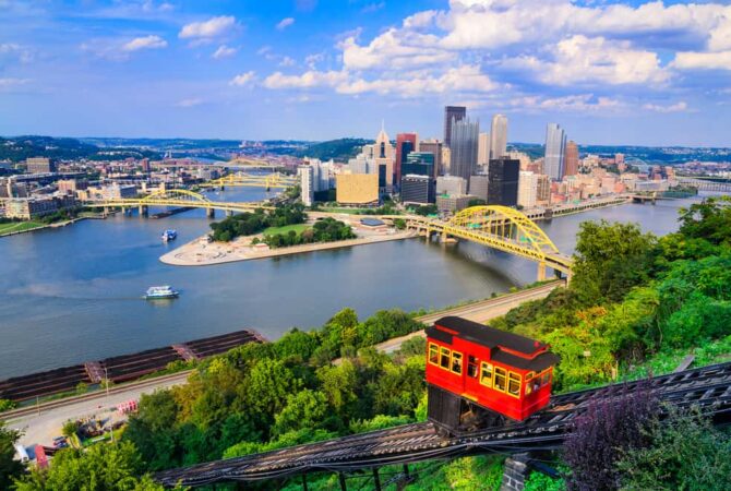A skyline view of Pittsburgh, PA with a semi-clear sky and the river surrounding the city.