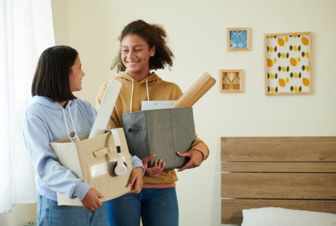 Two college students holding totes as they move into a dorm