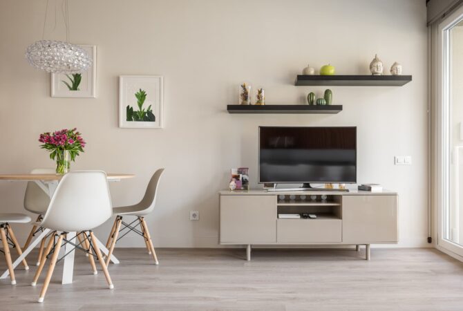 A clean living room with a Tv sand with some floating shelves with decor above the tv.